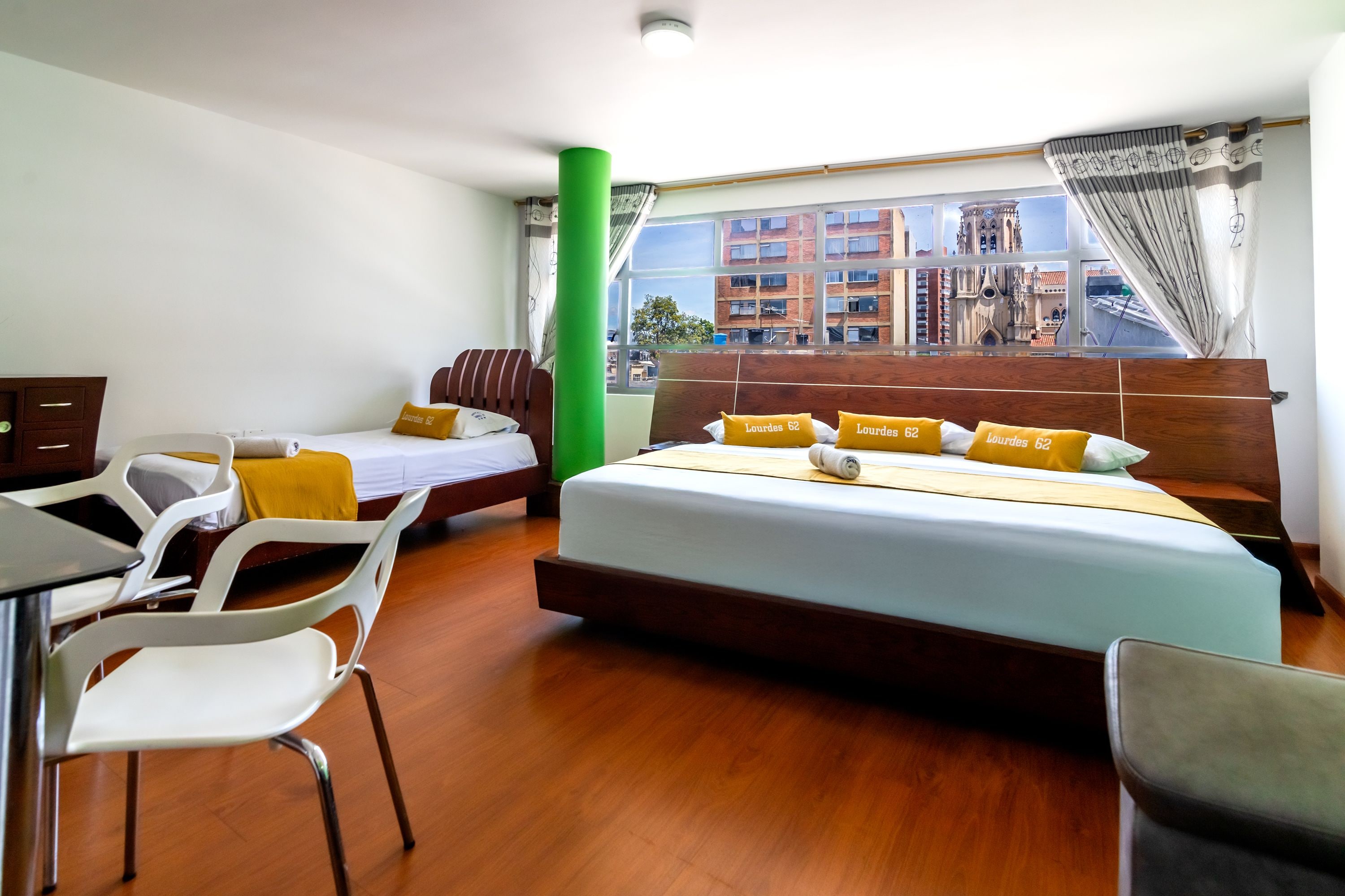 Une chambre d’hôtel avec un grand lit, deux fauteuils, un bureau et une fenêtre donnant sur des immeubles.