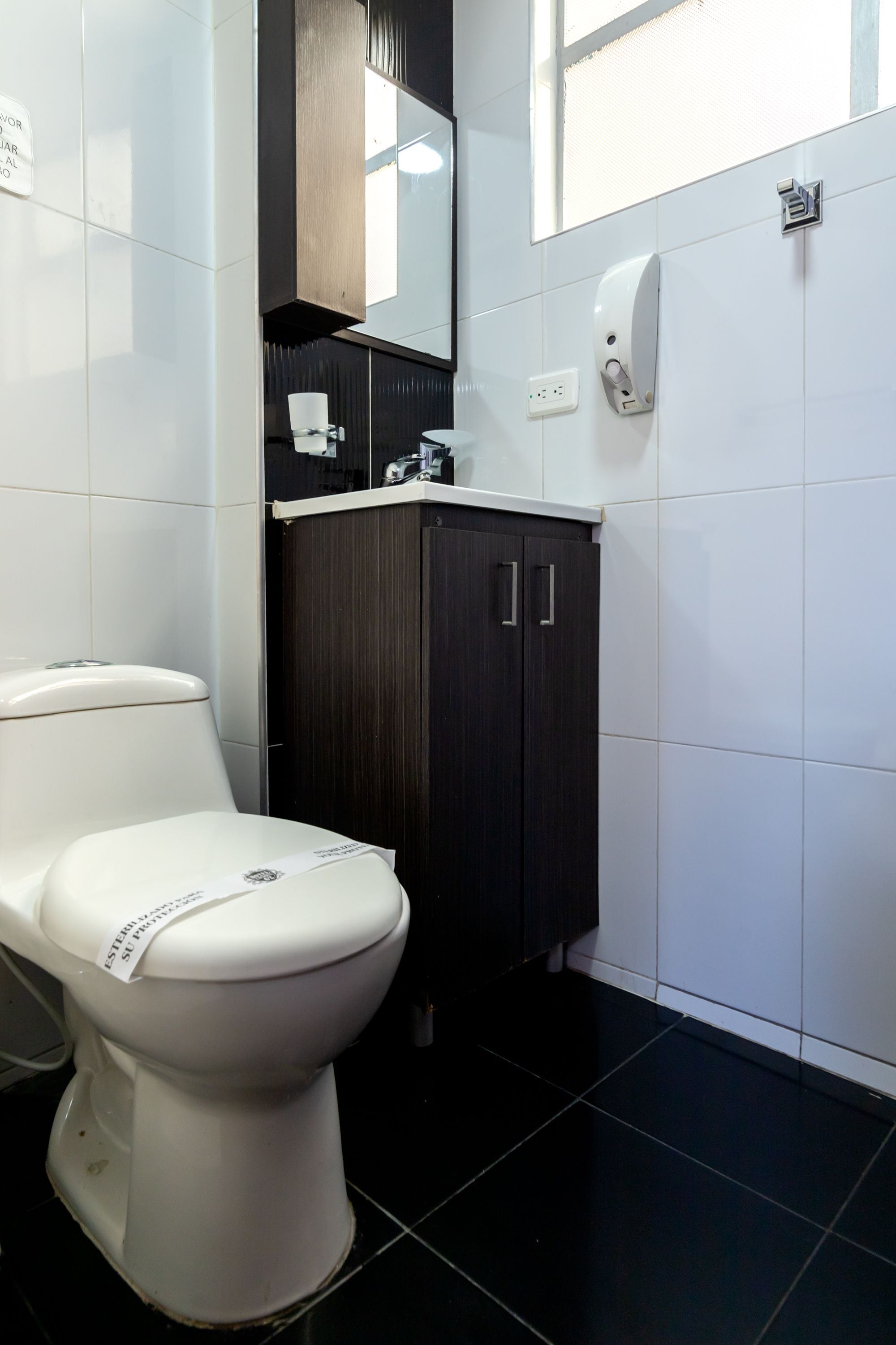 Un baño moderno con inodoro blanco, muebles de madera oscura y un lavamanos blanco.