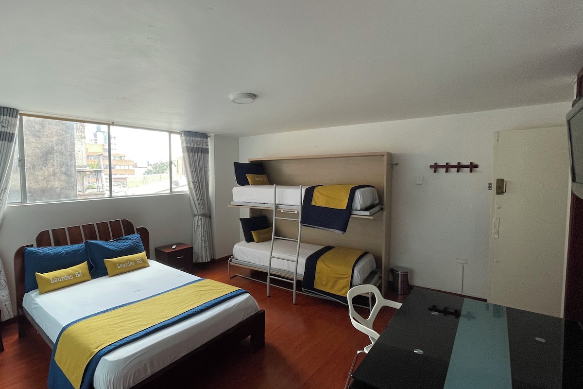 Habitación de hotel con una cama individual, una cama litera, suelo de madera, una ventana con cortinas, una mesita de noche y un teléfono.
