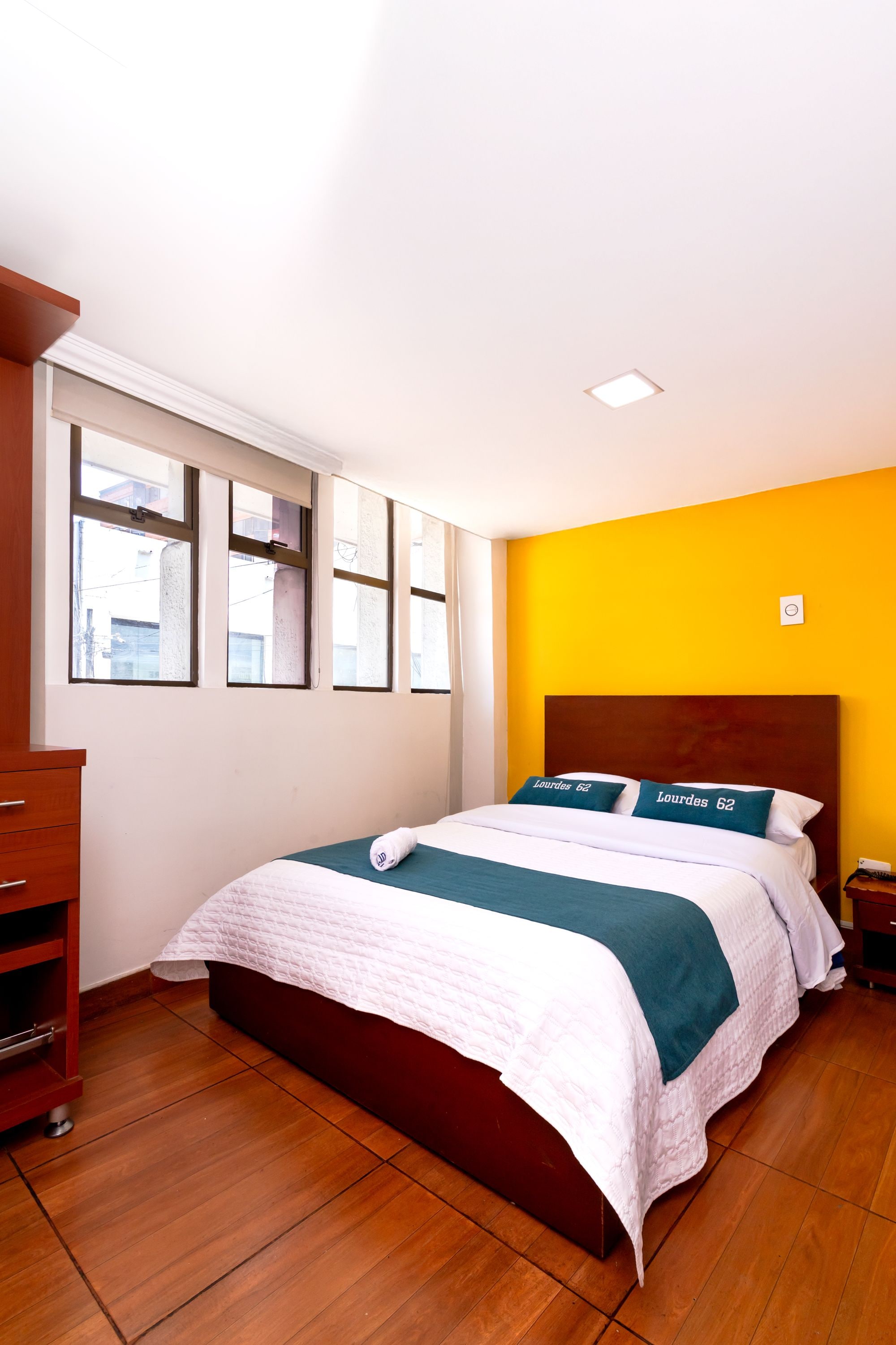 Une chambre d’hôtel avec un lit, une commode en bois et une fenêtre avec des stores.