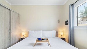 A hotel room with a bed, bedside lamps, a tray with a mug and a plate, and a window with curtains. - Aruba 1BR Apartment w Free Parking near Palm Beach (Noord)