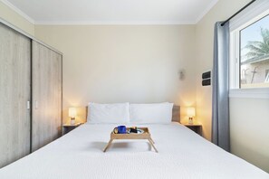 A hotel room with a bed, bedside lamps, a tray with a mug and a plate, and a window with curtains. - Aruba 1BR Apartment w Free Parking near Palm Beach (Noord)