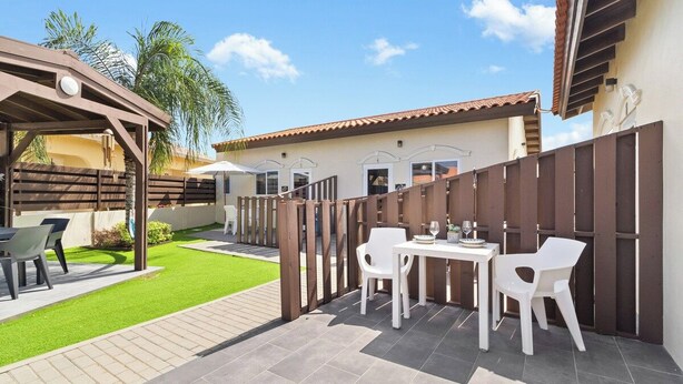 An outdoor patio area with a table and chairs, a pergola, and a fenced garden. - Aruba 1BR Apartment w Free Parking near Palm Beach (Noord)