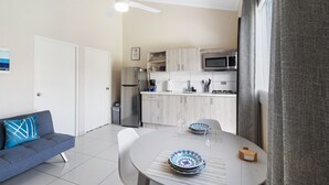 Una cocina moderna con armarios blancos, microondas y refrigerador. Hay una mesa de comedor con platos y una copa de vino.