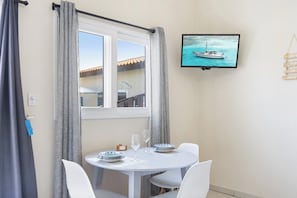 Ett rum med ett matbord för två personer, en tv som är monterad på väggen och ett fönster med gardiner.