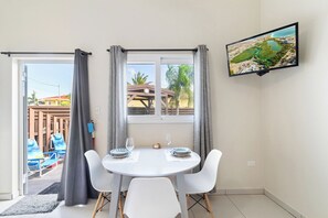 A room with a dining table set for two, a TV mounted on the wall, and a view of the outside.