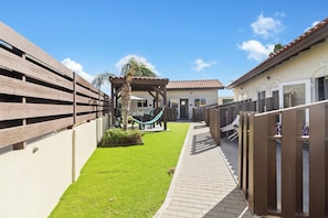 A fenced backyard with artificial grass, a hammock, and a patio area. - Aruba 1BR Apartment w Free Parking near Palm Beach (Noord)