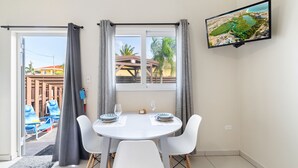 Una habitación con una mesa de comedor preparada para dos personas, un televisor en la pared y vistas al exterior a través de una ventana.