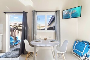 Ein Essbereich mit einem runden Tisch, zwei Stühlen, einem an der Wand montierten Fernseher und Blick auf ein Gebäude mit einem geneigten Dach.
