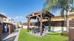 A patio area with a wooden pergola, a dining table with chairs, a hammock, and a small Christmas tree. - Little Seas #3 Aruba 1BR Apartment w Free Parking near Palm Beach (Noord)