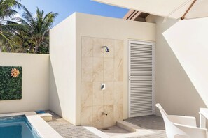 A modern outdoor shower area with a tiled wall, a showerhead, and a louvered door.