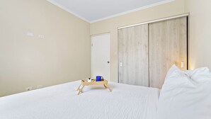 A bedroom with a bed, a wooden bedside table, a blue mug, and a tray with a cake and a candle. - Little Seas #3 Aruba 1BR Apartment w Free Parking near Palm Beach (Noord)