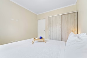 A bedroom with a bed, a wooden bedside table, a blue mug, and a tray with a cake and a candle. - Little Seas #3 Aruba 1BR Apartment w Free Parking near Palm Beach (Noord)