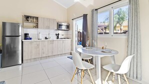 A modern kitchen with a refrigerator, microwave, and coffee maker, a dining area with a table and chairs, and a window with curtains. - Little Seas #3 Aruba 1BR Apartment w Free Parking near Palm Beach (Noord)