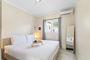 Ein Hotelzimmer mit einem Bett, einem Nachttisch mit Lampe, einem Fenster mit Vorhängen und einer Wand-Klimaanlage.