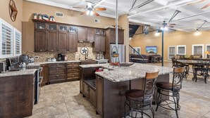 A spacious kitchen with dark wood cabinets, a granite countertop, and a large island with bar stools. - Family Getaway on the River | Pool, Sleeps 15, Spacious (Brazoria)
