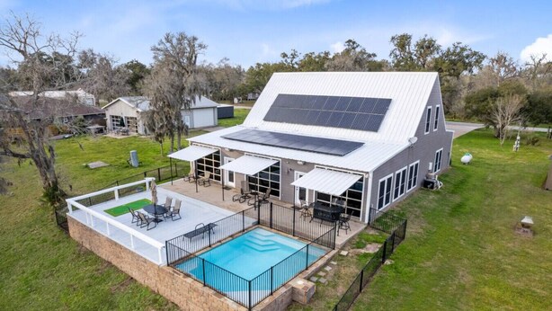 A modern house with a large swimming pool, solar panels, and a covered patio area. - Family Getaway on the River | Pool, Sleeps 15, Spacious (Brazoria)