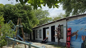 A playground with a seesaw and climbing structure, a mural of marine life, and a building with a tiled roof. - POSADA MISS ANIBEL  (San Andrés)