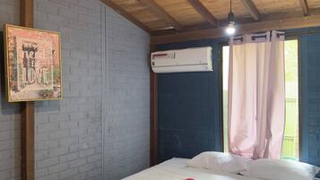 A bedroom with a wooden ceiling, a brick wall, a bed with white bedding, a red towel, and a framed picture.