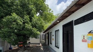 A courtyard with a white building, a tree, and colorful benches. - POSADA MISS ANIBEL  (San Andrés)