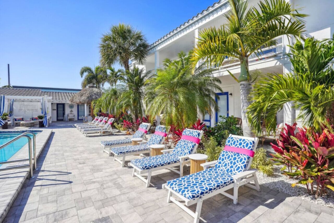 A poolside area with lounge chairs, palm trees, and a building with balconies.