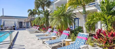 A poolside area with lounge chairs, palm trees, and a building with balconies.