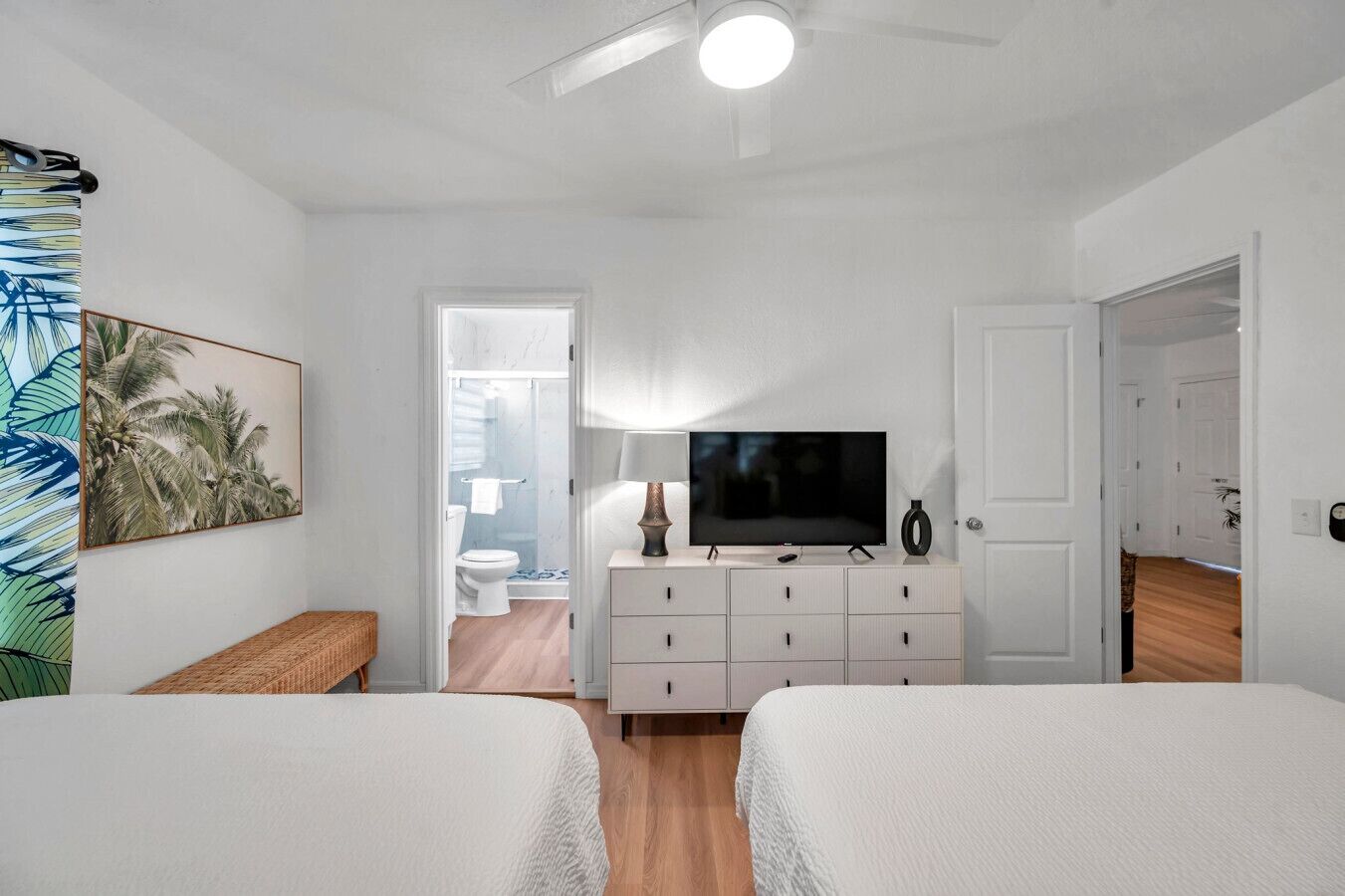 Een slaapkamer met twee bedden, een televisie, een dressoir en een badkamer die door een open deur zichtbaar is.