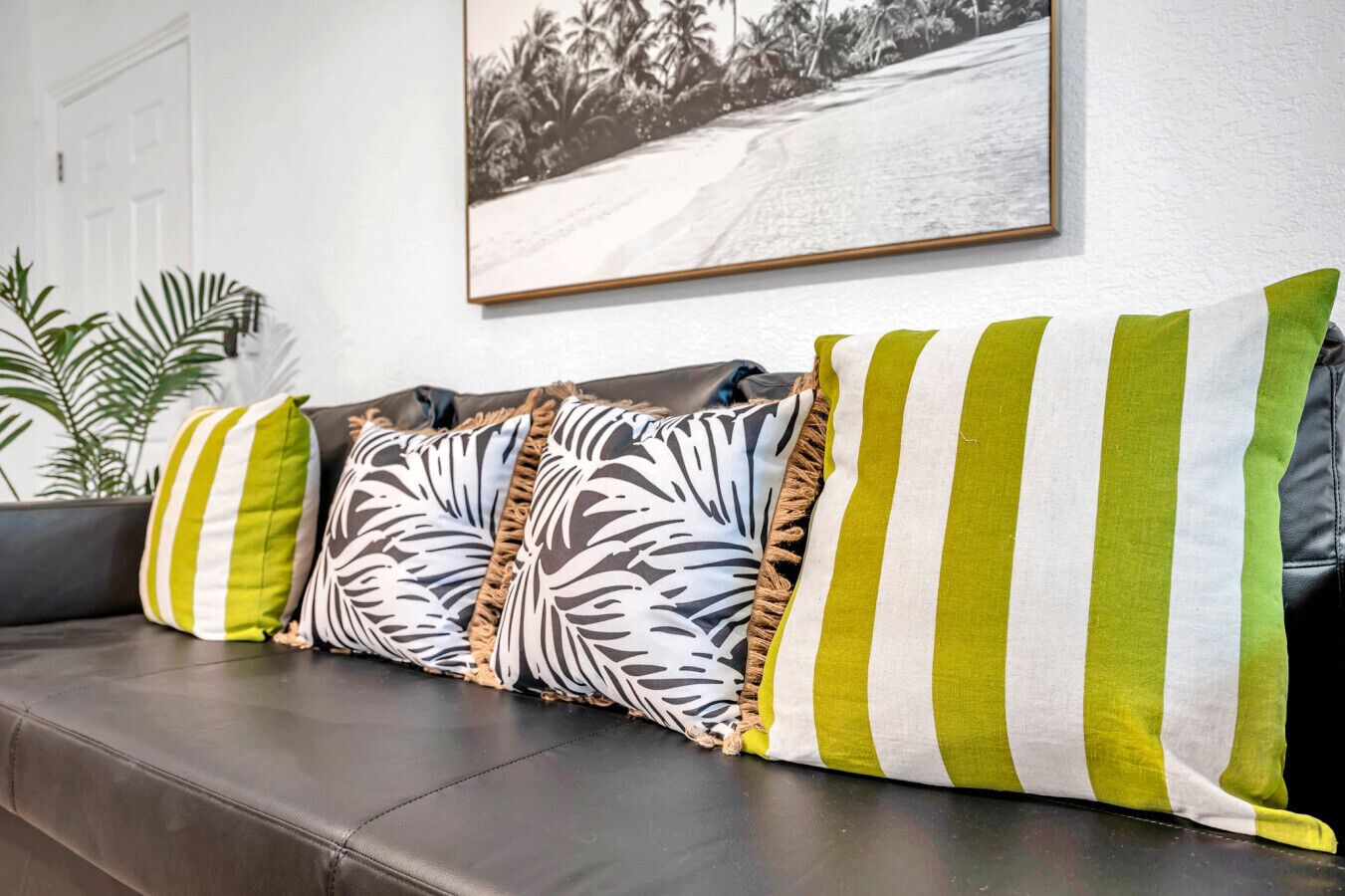 A dark leather sofa with striped pillows and a framed picture on the wall.