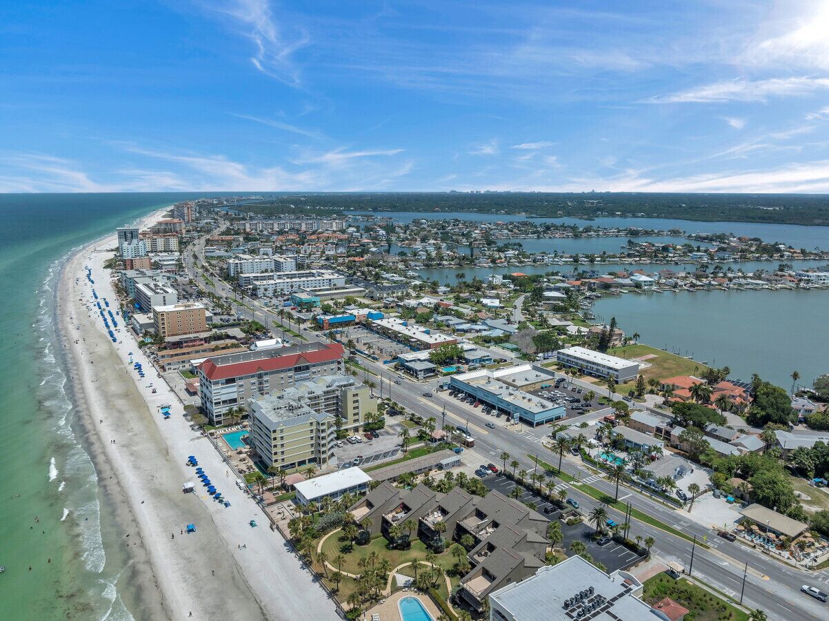 Vue aérienne d’une ville côtière avec une longue plage, une zone urbaine densément peuplée et un port de plaisance.