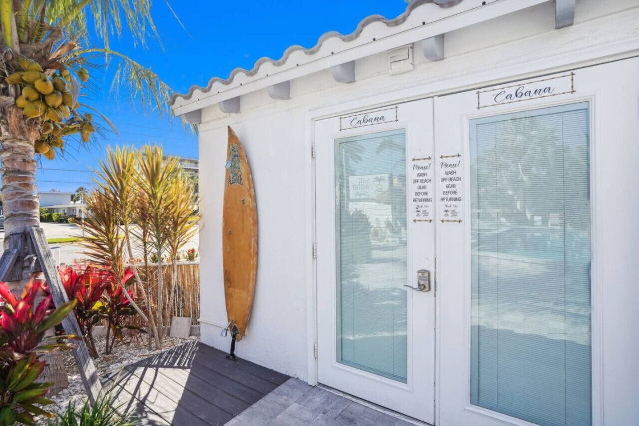 A white building with a glass door labeled "Cabana." A surfboard is leaning against the door.