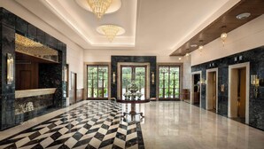 Un vestíbulo amplio con piso a cuadros, candelabros y una mesa de recepción.