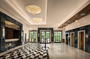 Un vestíbulo amplio con piso a cuadros, candelabros y una mesa de recepción.