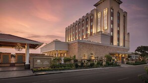 Un hotel moderno con una torre destacada, entrada cubierta y jardines bien cuidados.