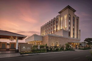 Un hotel moderno con una torre destacada, entrada cubierta y jardines bien cuidados.
