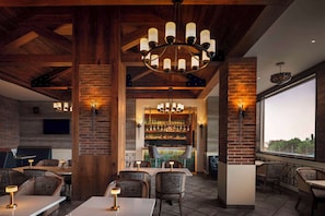 Un restaurante con paredes de ladrillo, vigas de madera y una zona de bar con estanterías llenas de botellas. Mesas y sillas dispuestas para comer.