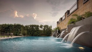 Una piscina con caída de agua, rodeada de un muro de piedra y vegetación.