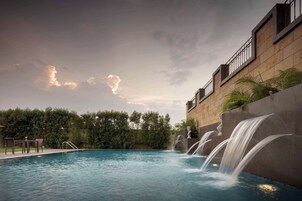 Una piscina con caída de agua, rodeada de un muro de piedra y vegetación.