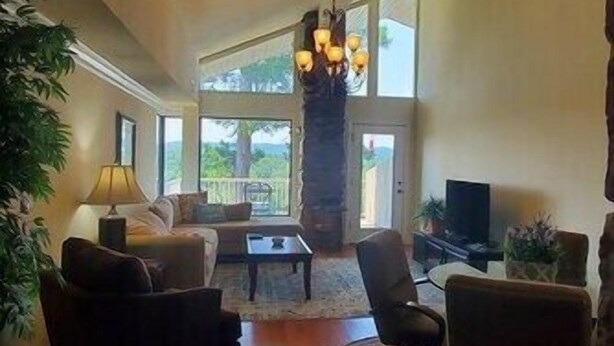 A spacious living room with a large chandelier, a sofa, armchairs, and a coffee table. There is a television and a potted plant. - Lake Views from this Balcony are amazing! (Hot Springs)