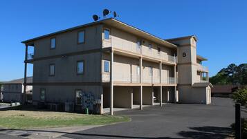 A multi-story building with a flat roof, balconies, and a parking area in front.