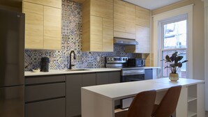 A modern kitchen with wooden cabinets, a tiled backsplash, a stainless steel refrigerator, a microwave, and a stove.