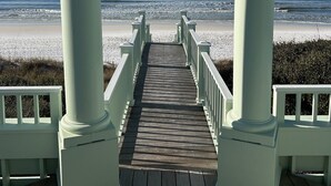 A wooden pier leading to a beach with white columns and railings.