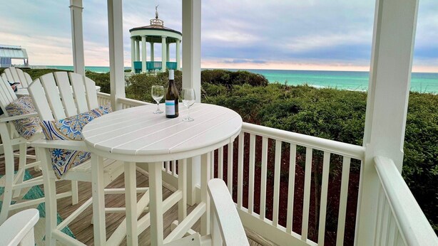 A covered outdoor seating area with a table, chairs, and a bottle of wine.
