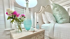 A bedroom with a bed, a bedside table with a vase of flowers, a water bottle, and a lamp.