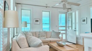 A coastal living room with a beige sofa, a woven coffee table, and a ceiling fan.