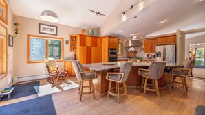 A modern kitchen with wooden cabinets, a central island with bar stools, and a large window providing natural light. - Peak 7, dog friendly fenced in yard, hot tub, pool table & dedicated work space (Breckenridge)