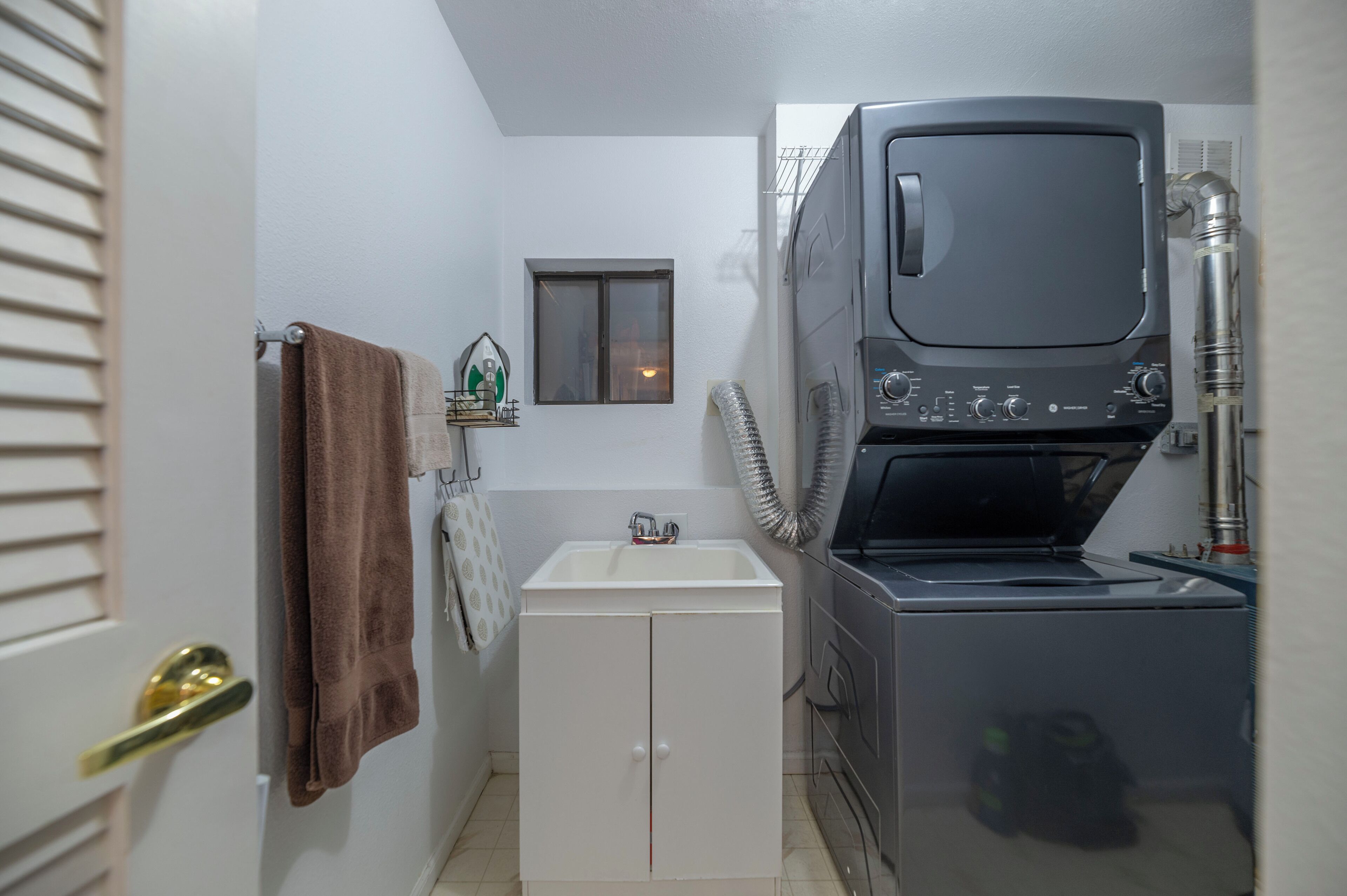 A compact laundry room with a washing machine, a small window, and a towel rack.