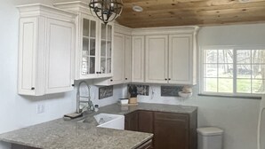 Cucina con mobili bianchi, piano di lavoro in granito, soffitto in legno e lampadario a sospensione.