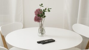 Une table ronde blanche, sur laquelle se trouvent un vase de fleurs et une télécommande.