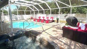 A covered outdoor area with a hot tub, red lounge chairs, and a pool.
