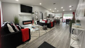 A modern living room with a fireplace, a sofa, a coffee table, and a kitchen area in the background.